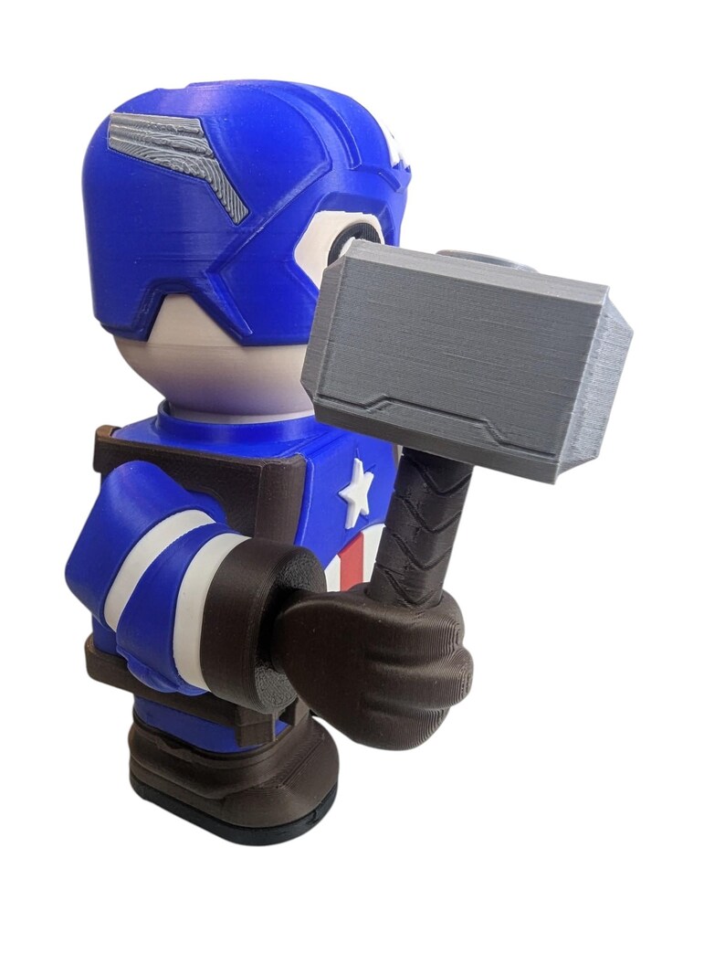May include: A blue and brown Captain America figurine holding a gray hammer. The figurine has a blue helmet with silver accents, a white star on the chest, and white stripes on the arms. The hammer is gray with a textured handle.