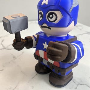 May include: A 3D-printed Captain America figurine holding a gray hammer. The figurine is primarily blue, with white and red accents, and a white star on the chest. The helmet has a white "A" on the forehead.