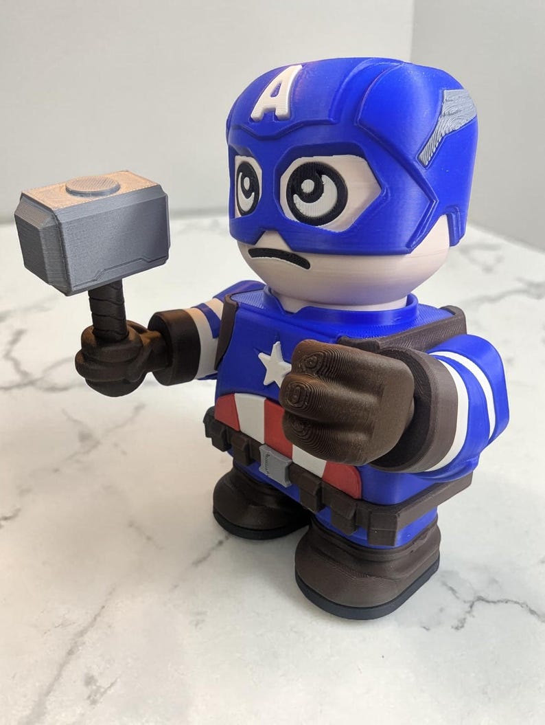 May include: A 3D-printed Captain America figurine holding a gray hammer. The figurine is primarily blue, with white and red accents, and a white star on the chest. The helmet has a white "A" on the forehead.