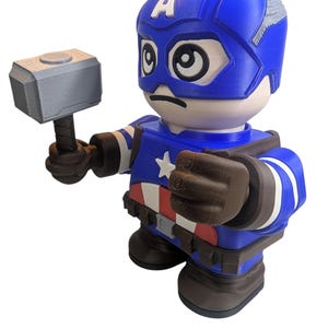 May include: A blue and white Captain America figurine holding a silver hammer. The figurine has a blue helmet with the letter "A" on the forehead, a star on the chest, and a red, white, and blue belt. The figurine is a collectible item.