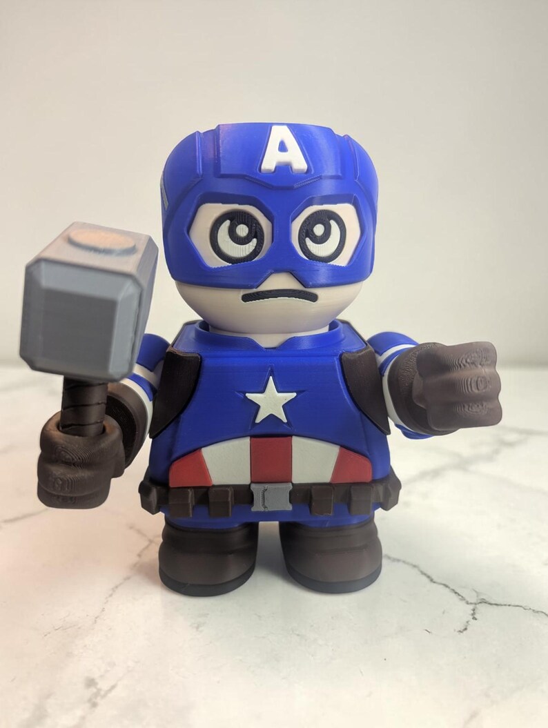 May include: A blue and white Captain America figurine holding a gray hammer. The figurine has a blue helmet with a white "A" and a white star on the chest. The figure is wearing a blue and white costume with brown gloves and boots.