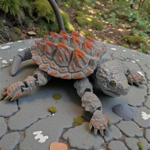 May include: A gray and orange toy ankylosaurus dinosaur with articulated limbs and a textured shell. The toy is positioned on a gray, stone-like surface with a natural background of greenery.