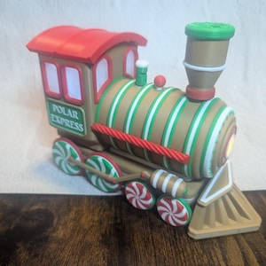 May include: A decorative train with a red roof, brown body, and green and white striped accents. The train wheels and smokestack have a candy cane design. The words "POLAR EXPRESS" are printed on the side.