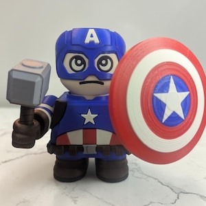 May include: A blue, red, and white Captain America figurine holding a hammer and shield. The figurine has a blue helmet with the letter "A" on it, a star on the chest, and a red, white, and blue shield.