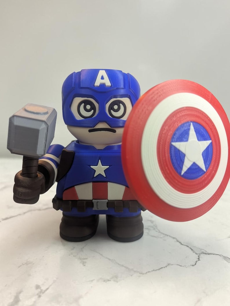 May include: A blue, red, and white Captain America figurine holding a hammer and shield. The figurine has a blue helmet with the letter "A" on it, a star on the chest, and a red, white, and blue shield.