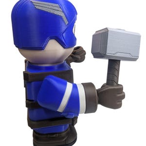 May include: A blue and white figurine of a superhero holding a gray hammer. The figurine has a blue helmet with a silver design, a blue suit with white stripes, and brown gloves and boots. The hammer is gray with a brown handle.