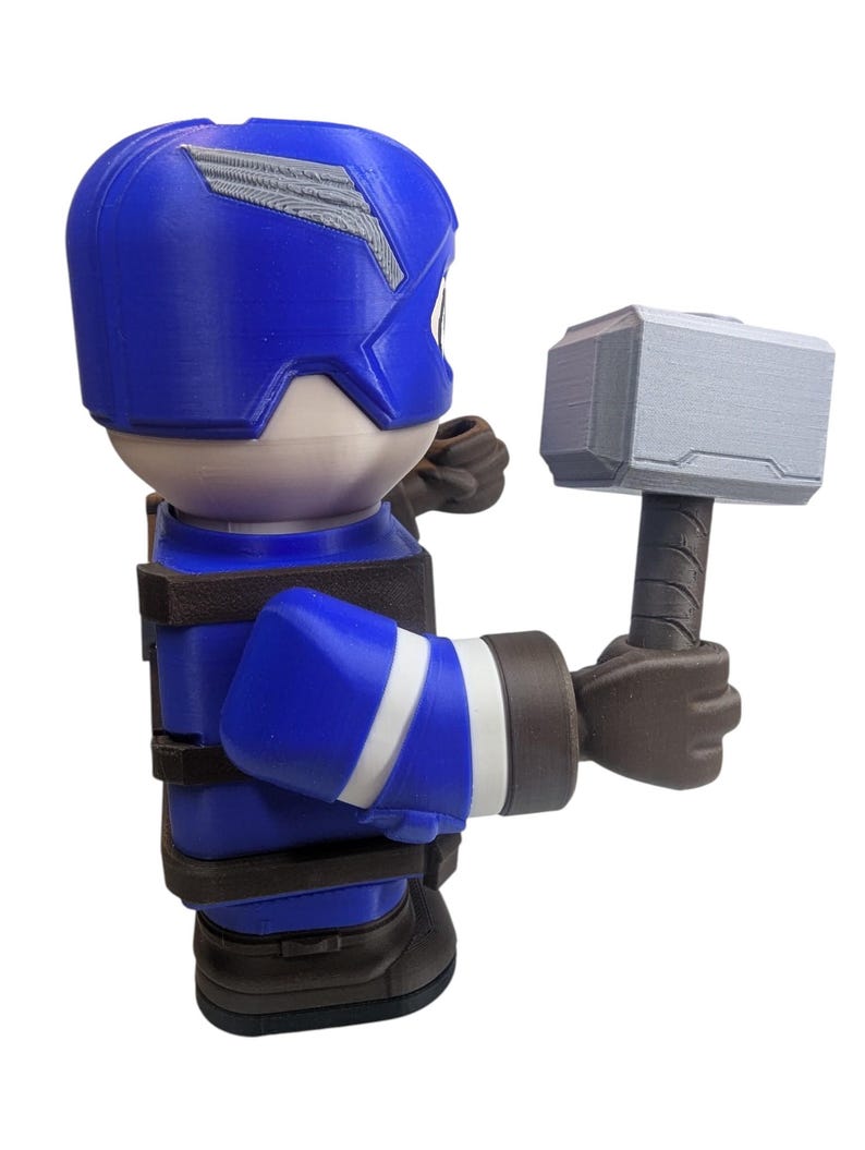 May include: A blue and white figurine of a superhero holding a gray hammer. The figurine has a blue helmet with a silver design, a blue suit with white stripes, and brown gloves and boots. The hammer is gray with a brown handle.