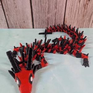 May include: A red and black articulated dragon toy with a spiky design. The dragon is made of plastic and has a segmented body.