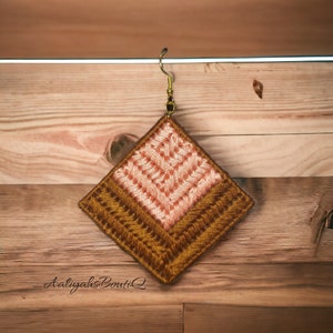 May include: A pair of handmade earrings with a geometric design. The earrings are made of brown and pink fabric and have a gold hook.