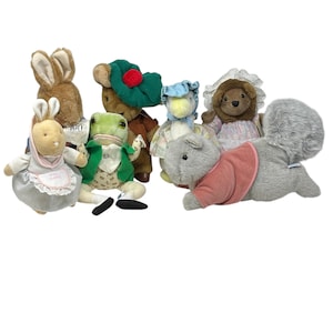 Könnte beinhalten: Eine Sammlung von Plüschtier-Spielzeugen, darunter ein braunes Kaninchen, ein Frosch in einer grünen Jacke, eine Ente mit Hut, ein Bär und ein graues Eichhörnchen mit rosa Weste. Die Spielzeuge sind weich und detailliert, mit verschiedenen Outfits und Accessoires.