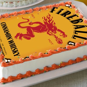 May include: A white cake with orange frosting and sprinkles. The cake is decorated with a printed image of a Fireball Cinnamon Whisky bottle label. The label features a red demon with flames and the text "Fireball", "Red", "Hot", and "Cinnamon Whisky".