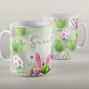 Może przedstawiać: Biały kubek ceramiczny z wzorem zielonych, r&oacute;żowych i niebieskich jajek wielkanocnych. Kubek ma napisane imię "Sara" czarnym, ozdobnym pismem.