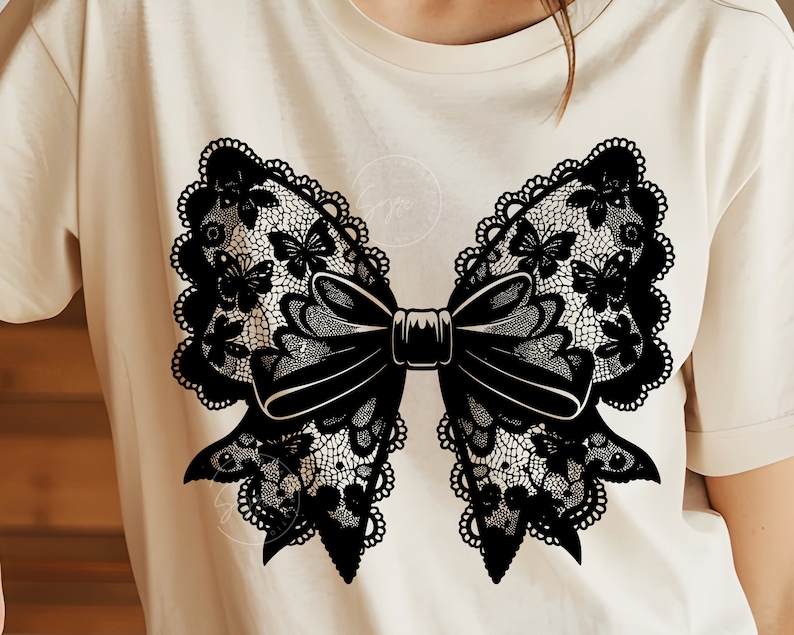 May include: A black lace bow with butterfly details on a white t-shirt.
