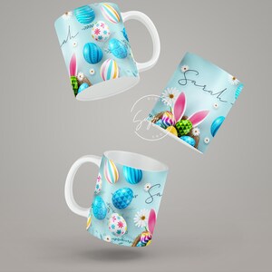 May include: Two white ceramic mugs with a blue background and colorful Easter eggs, one mug says "Sarah" on it.