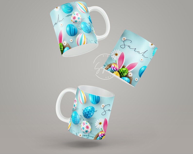 May include: Two white ceramic mugs with a blue background and colorful Easter eggs, one mug says "Sarah" on it.