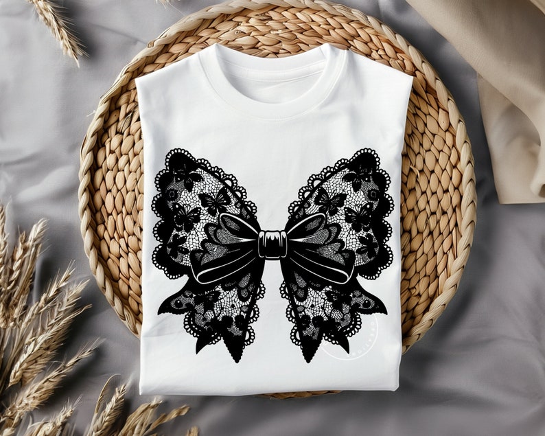 May include: A white t-shirt with a black lace bow design. The bow is made of intricate lace with a floral pattern and a center bow.