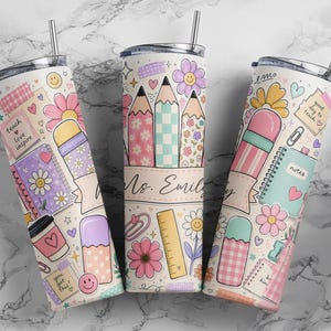 May include: Three cylindrical tumblers with metal straws featuring a repeating pattern of school supplies, flowers, and hearts in pastel colors. The design includes illustrations of pencils, a ruler, notebooks, and text reading teach love inspire.