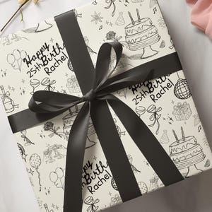 May include: White gift wrap with a black ribbon. The wrap has a repeating pattern of birthday party doodles, including balloons, cake, and champagne glasses. The text "Happy 25th Birth Rachel" is written on the wrap.