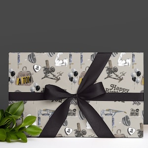 May include: A wrapped gift with a black bow. The wrapping paper has a beige background with illustrations of gym equipment, balloons, and the text "I love you a ton" and "Happy Birthday".