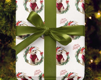 May include: Wrapped gift with festive Christmas-themed wrapping paper featuring a repeating pattern of a dog wearing a Santa hat and red sweater, surrounded by a wreath. A green ribbon and bow complete the presentation. The words "Merry Christmas" are also printed on the wrapping paper.