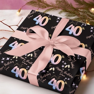 May include: A wrapped gift with black paper featuring the number "40" in pastel colors, champagne glasses, and stars. A light pink ribbon and bow adorn the gift. The words "Happy Birthday Sara" are also printed on the wrapping paper.