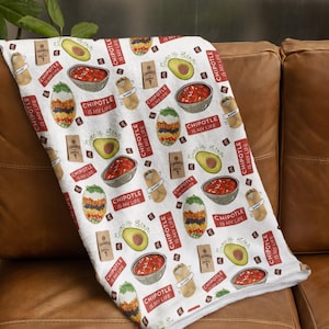 May include: White fleece blanket with a repeating pattern of Chipotle restaurant food items, including bowls, burritos, guacamole, and salsa. The text "Chipotle is my life" is repeated throughout the pattern.