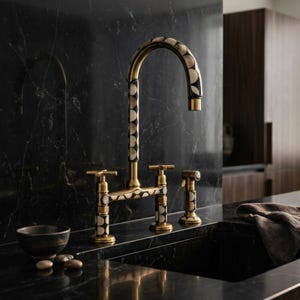 Puede incluir: Un grifo de cocina de arco alto con acabado en latón y un patrón circular repetido en blanco y negro en el caño, la base y el rociador lateral. El grifo cuenta con dos manijas en forma de cruz y está montado sobre una encimera de mármol negro.