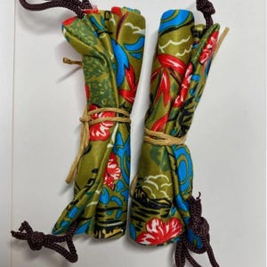 May include: Two rolled fabric items with a floral pattern in green, red, and blue. Each is tied with natural twine and has a dark brown cord attached. The fabric has a botanical design.