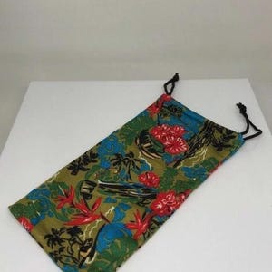 May include: A rectangular drawstring pouch with a tropical floral design. The fabric displays red hibiscus flowers, blue accents, and palm trees on a green backdrop. Black drawstrings secure the top.