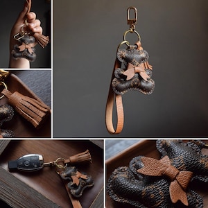 K&ouml;nnte beinhalten: Brauner Leder-Schl&uuml;sselanh&auml;nger mit Teddyb&auml;r-Design und Schleife. Der Schl&uuml;sselanh&auml;nger hat einen goldfarbenen Verschluss und eine passende Lederquaste. Der B&auml;r hat ein strukturiertes Muster und einen kleinen Lederriemen.
