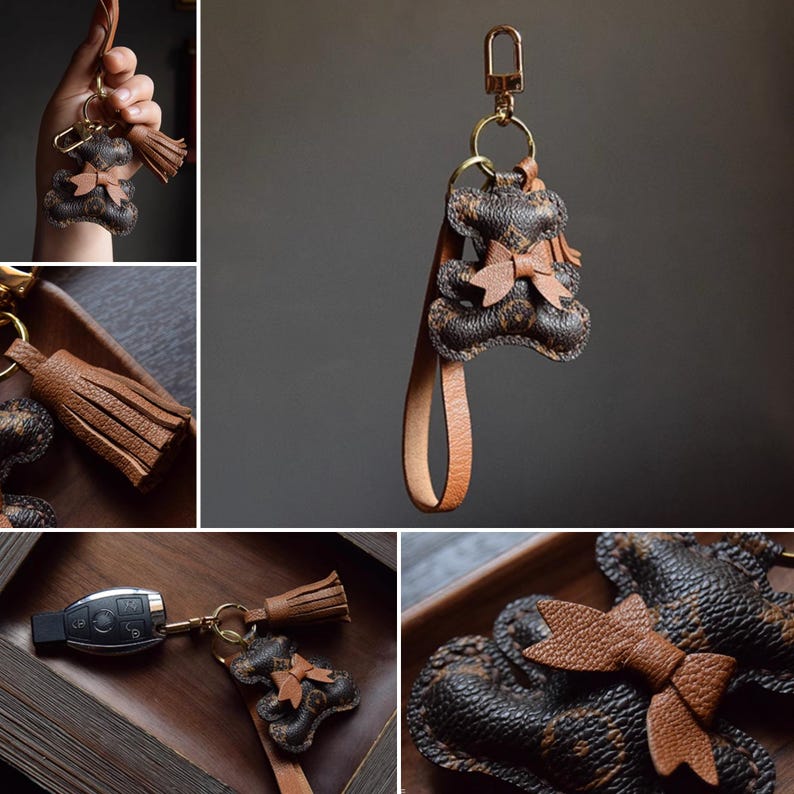 K&ouml;nnte beinhalten: Brauner Leder-Schl&uuml;sselanh&auml;nger mit Teddyb&auml;r-Design und Schleife. Der Schl&uuml;sselanh&auml;nger hat einen goldfarbenen Verschluss und eine passende Lederquaste. Der B&auml;r hat ein strukturiertes Muster und einen kleinen Lederriemen.