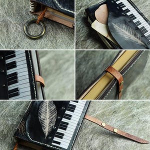 Pu&ograve; includere: Un diario in pelle nera con un design a tastiera di pianoforte e un'impronta di foglia. Il diario ha una chiusura con cinturino in pelle marrone e un anello di metallo. Le pagine sono ingiallite e le cuciture sono bianche.