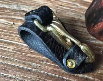 May include: A black leather bracelet with a gold metal clasp. The clasp is a hook and eye design.