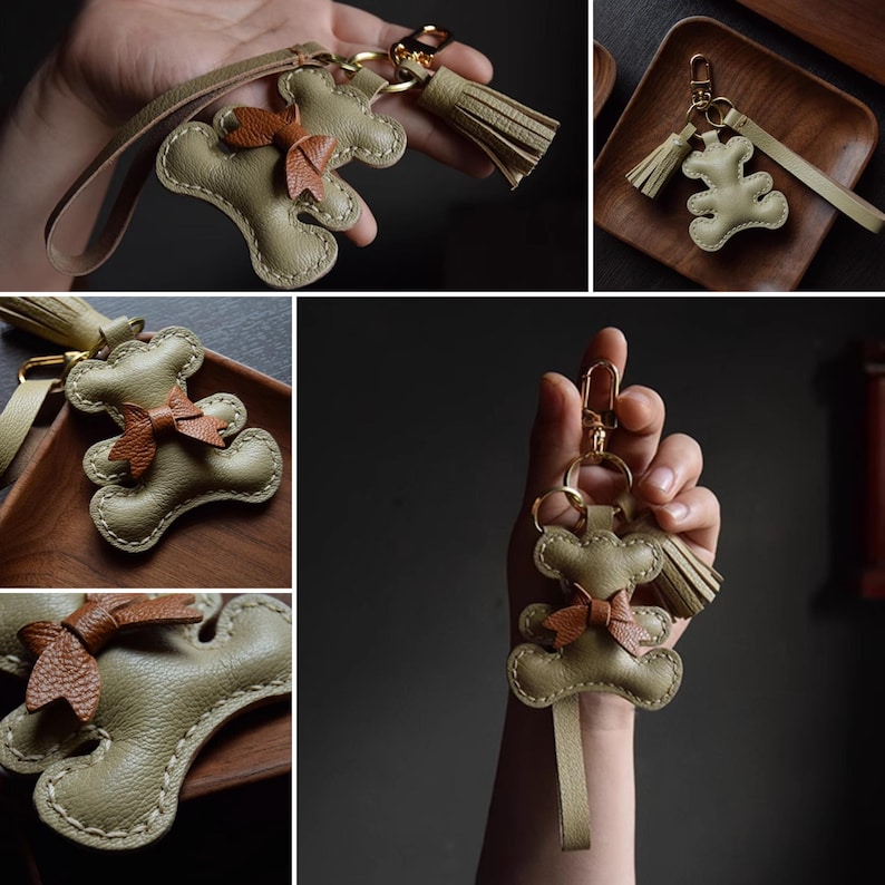 K&ouml;nnte beinhalten: Handgefertigter Leder-Schl&uuml;sselanh&auml;nger in Form eines Teddyb&auml;ren. Der Schl&uuml;sselanh&auml;nger ist olivgr&uuml;n mit einer braunen Schleife und Quaste. Die N&auml;hte sind sichtbar, und die Hardware ist goldfarben.