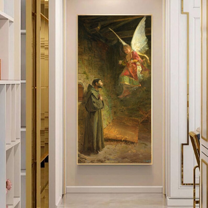 May include: A framed painting depicting a religious scene. A man in a brown robe stands in a stone room, looking up at an angel with large white wings. The angel is wearing a red and gold garment. The painting has a gold frame.