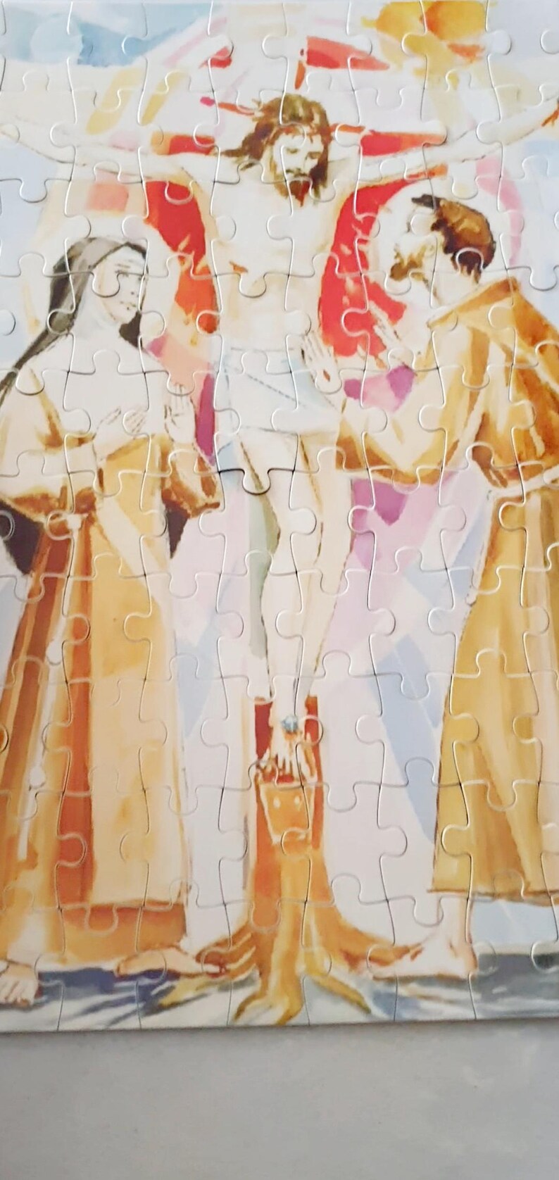 May include: A completed jigsaw puzzle depicting a religious scene. The image features a central figure on a cross, flanked by two other figures. The puzzle pieces are interlocked, forming a cohesive image with muted colors.