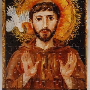 May include: A completed jigsaw puzzle featuring a religious figure with a halo. The puzzle depicts a man in brown robes with a beard, hands raised, and a golden halo. The puzzle is supported by two silver stands.