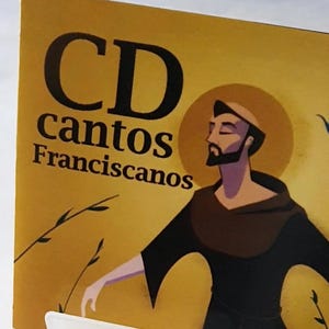 May include: A CD case with the words "CD cantos Franciscanos" in black lettering on a yellow background. The image features an illustration of a man in a brown robe with a halo. The CD case is propped up by a white stand.