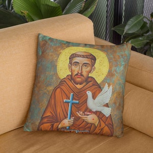 May include: A throw pillow with a vintage-style illustration of Saint Francis of Assisi holding a dove. The background is a textured, green, brown, and gold color.