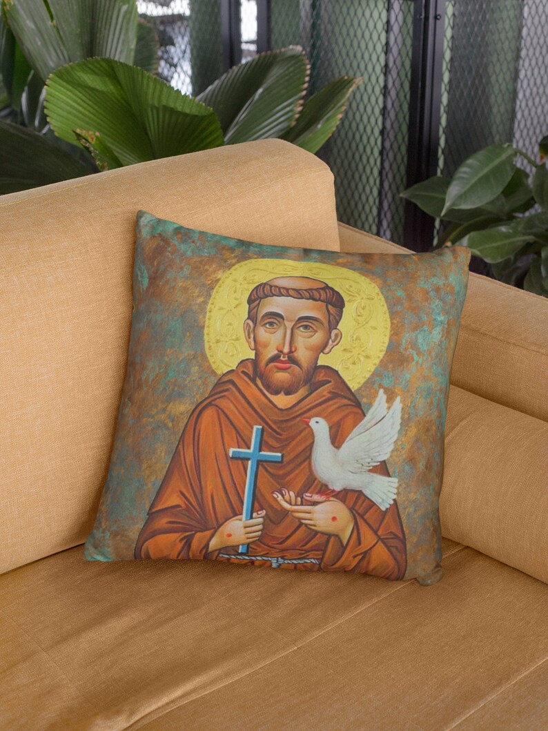 May include: A throw pillow with a vintage-style illustration of Saint Francis of Assisi holding a dove. The background is a textured, green, brown, and gold color.