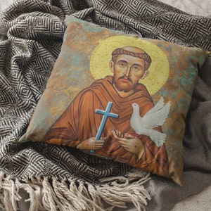 May include: A throw pillow with a vintage-style illustration of Saint Francis of Assisi. The image features Saint Francis holding a dove and a cross, with a halo behind his head. The background is a faded blue and green.