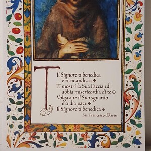K&ouml;nnte beinhalten: Ein gerahmter Druck mit einer Illustration eines Mannes mit Heiligenschein, vor blauem Hintergrund. Der Druck enth&auml;lt italienischen Text und ist von einem dekorativen floralen Rand umgeben.