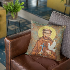 May include: A brown leather couch with a throw pillow featuring a painting of Saint Francis of Assisi holding a dove and a cross. The pillow is on a gray throw pillow.