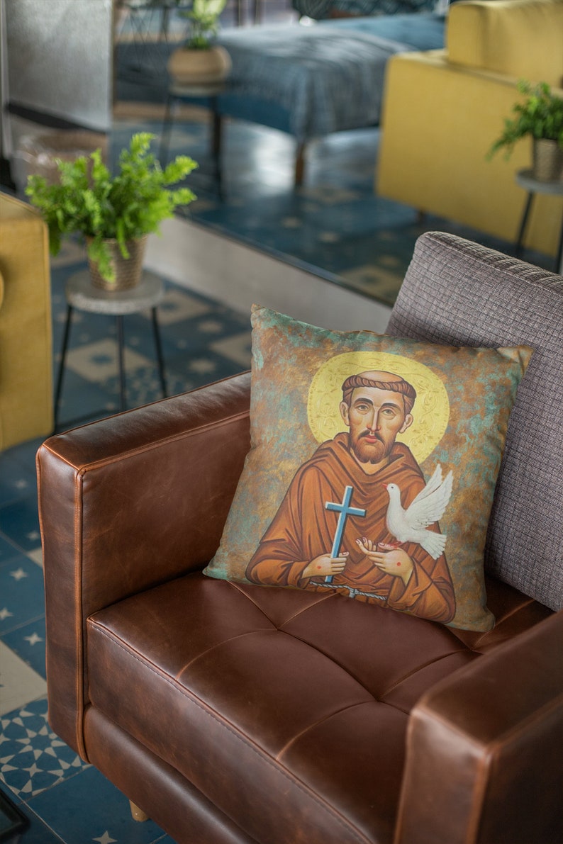 May include: A brown leather couch with a throw pillow featuring a painting of Saint Francis of Assisi holding a dove and a cross. The pillow is on a gray throw pillow.