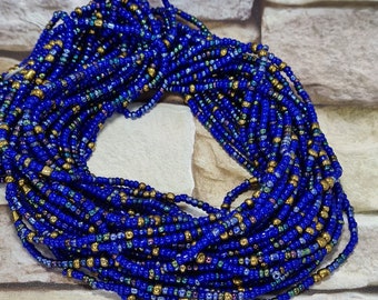 May include: A close-up of a blue and gold beaded necklace. The beads are small and round, and they are arranged in a pattern of blue and gold. The necklace is coiled up and is lying on a stone surface.