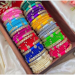 Peut inclure: Une pile de bracelets en fil de soie colorés avec des embellissements en pierres précieuses. Les bracelets sont disposés dans une boîte en bois.