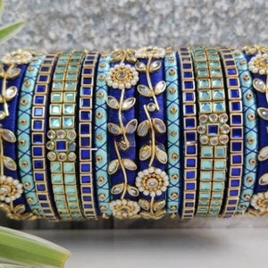 Può includere: Un set di braccialetti blu e blu chiaro con decorazioni dorate e bianche. I braccialetti sono decorati con motivi floreali e strass.