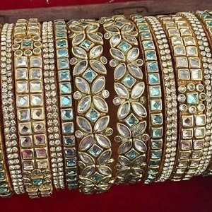 May include: A set of gold bangles with intricate designs featuring blue and clear gemstones. The bangles are stacked together in a display.