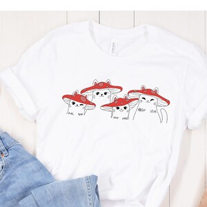 May include: White t-shirt with a graphic of four cats wearing red mushroom hats. The text on the shirt reads "I love you" and "meow meow".