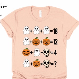 May include: A light pink t-shirt with a Halloween-themed math problem. The problem features ghosts, pumpkins, and a skull. The equation is: Ghost + Ghost + Ghost = 18, Ghost + Pumpkin + Pumpkin = 12, Pumpkin + Ghost - Skull = 4, Ghost + Pumpkin x Skull = ?